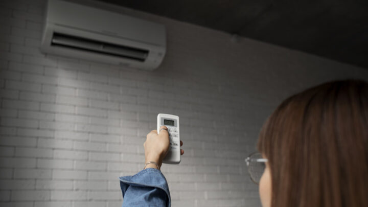 Mulher a controlar um ar condicionado com o comando