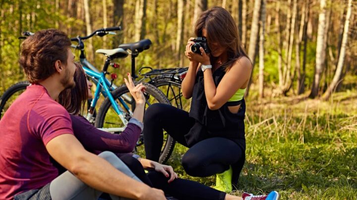 Pessoas a aproveitarem tempo livre na floresta. Uma rapariga tira uma fotografia, com uma máquina a duas outras pessoas.