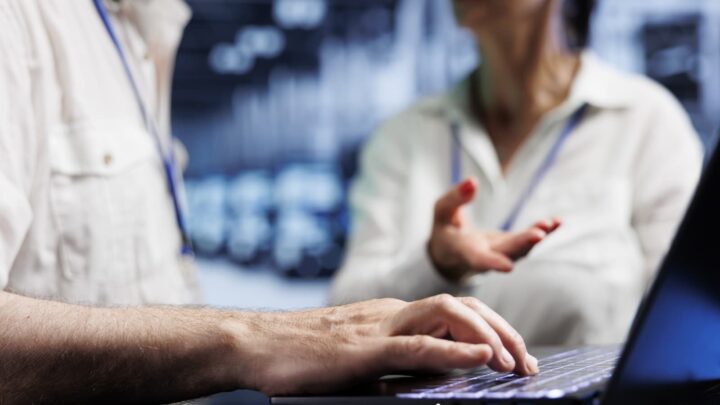 Pessoas de TI a explicar algo a outra, com um computador entre ambas