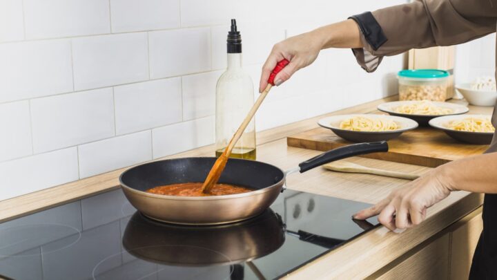 Placa de indução, com um tacho em cima e uma pessoa a cozinhar