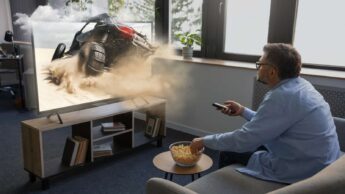 Homem sentado no sofá a ver televisão, com uma taça de pipocas em cima de uma mesa.