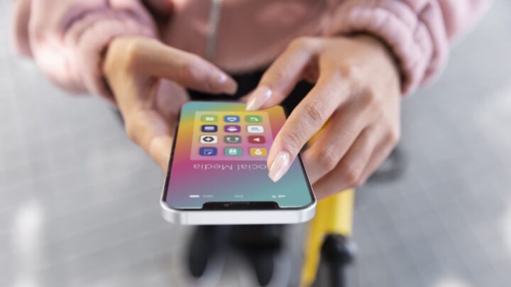Pessoa a segurar num smartphone, de frente, com ícones de redes sociais