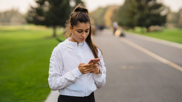Rapariga parada com o smartphone, com roupa de corrida