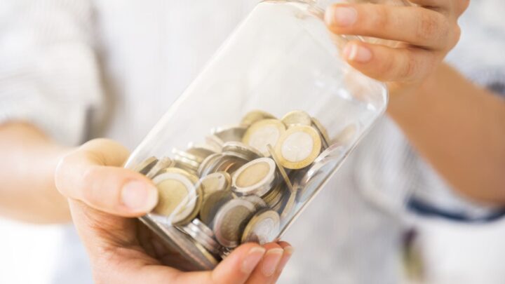 Pessoa a segurar num frasco transparente de moedas