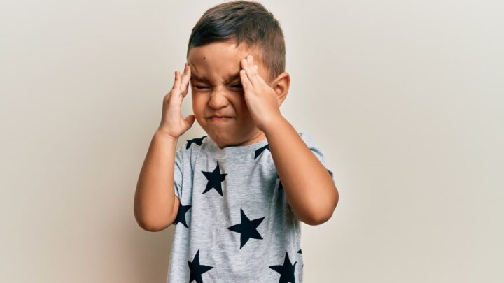 Criança com as mãos a pressionas as têmporas, com dor de cabeça
