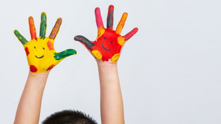Criança a representar o dia da criança, com as mãos pintadas. Um sorriso em cada uma delas.