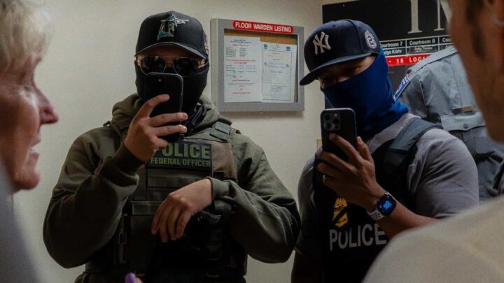 Dois agentes do ICE filmam a imprensa com smartphones no corredor em frente ao tribunal de imigração, na cidade de Nova Iorque, no dia 11 de julho de 2025. Crédito: Madison Swart/Getty Images, via <a href="https://www.politico.com/news/2026/02/06/dhs-inspector-general-investigates-ice-surveillance-00768778">POLITICO</a>